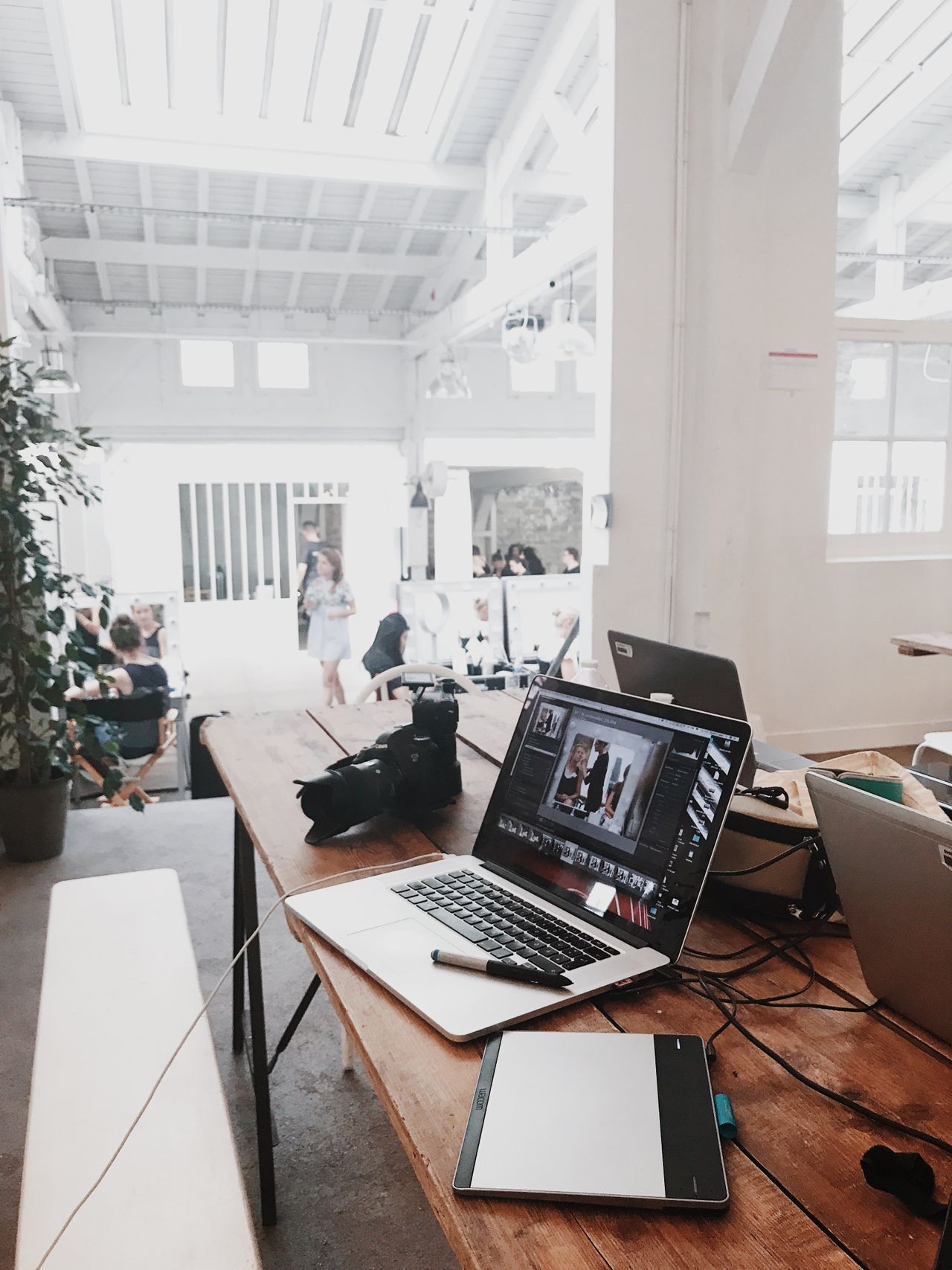 Open-space studio desk with a laptop displaying photo editing software, a DSLR camera, and a Wacom tablet fot. PEXELS