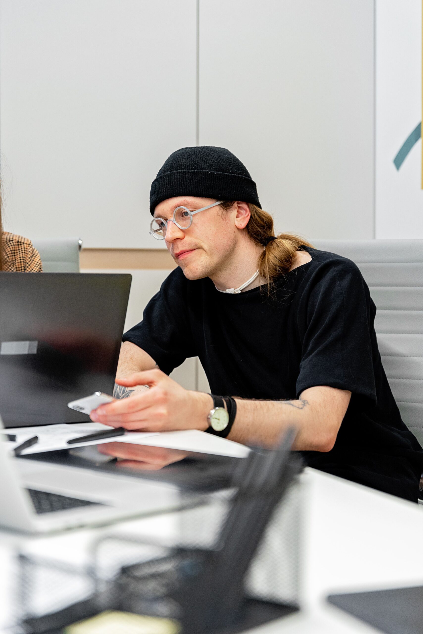 Male designer in a beanie and glasses discussing a project at a London studio meeting fot. PEXELS