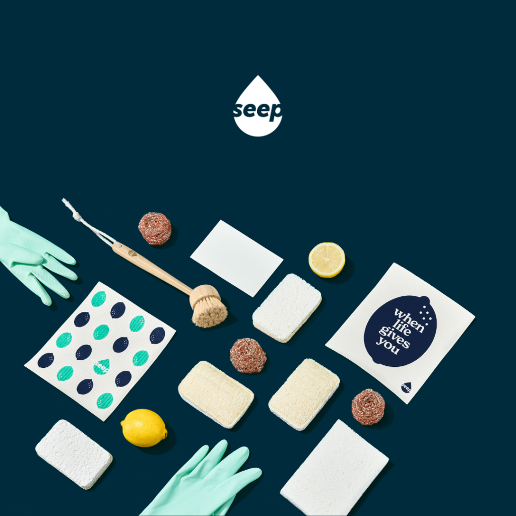 Top-down flatlay of eco-friendly sponges, brushes, lemons, and branded packaging on a navy background